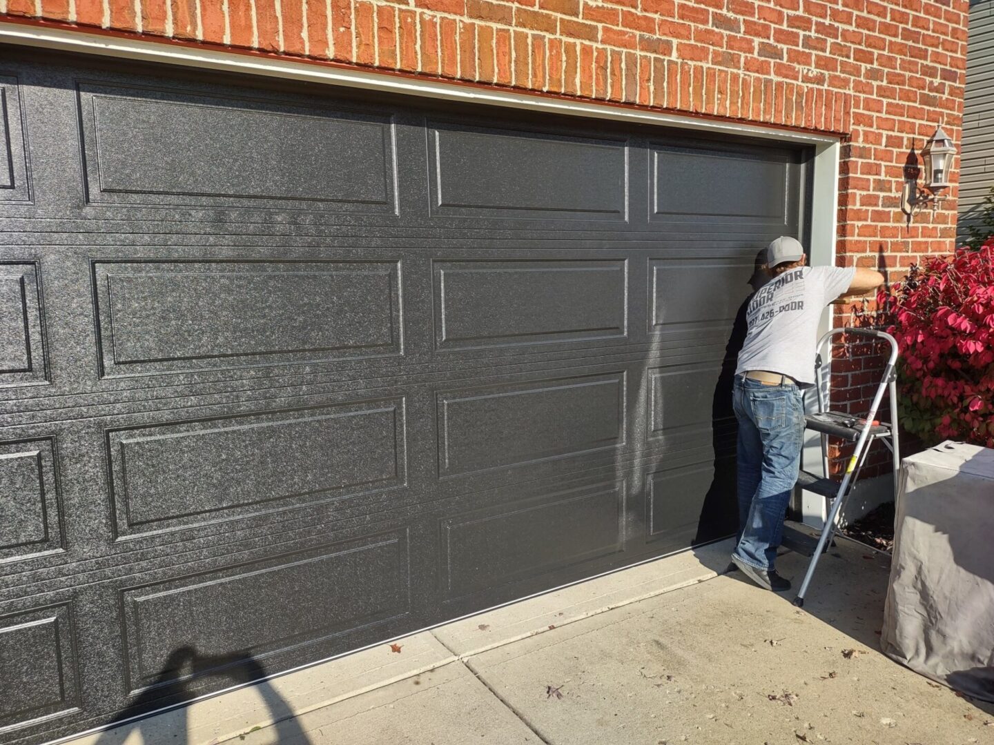 Man repairing a black garage door next to a brick wall.